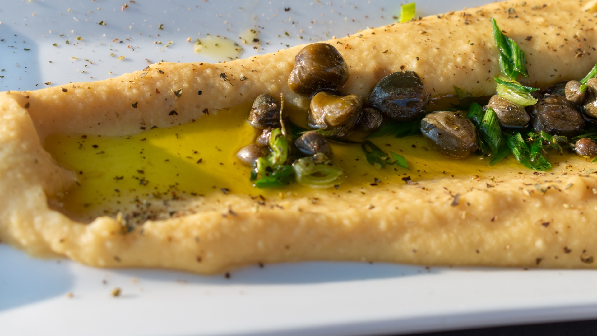 A close up of Fava puree topped with olive oil and capers. 