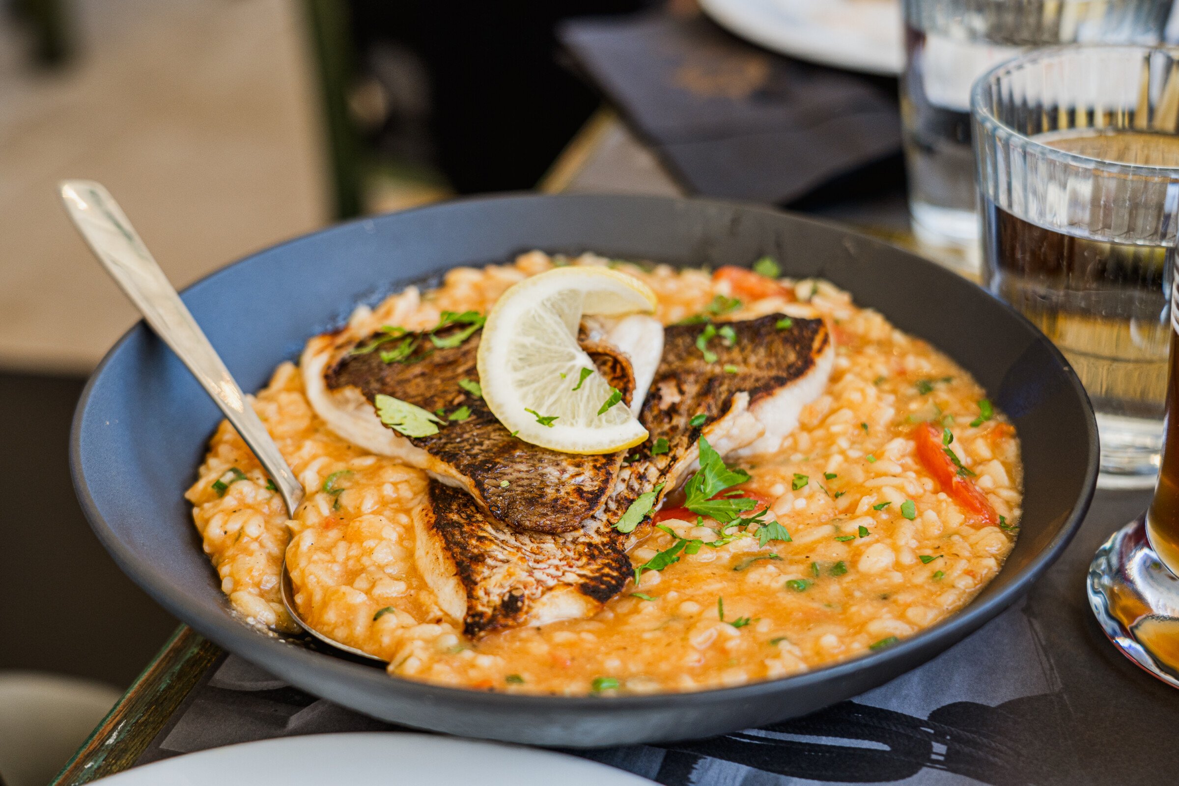 A dark grey plate with Risotto topped with two pieces of fish. 