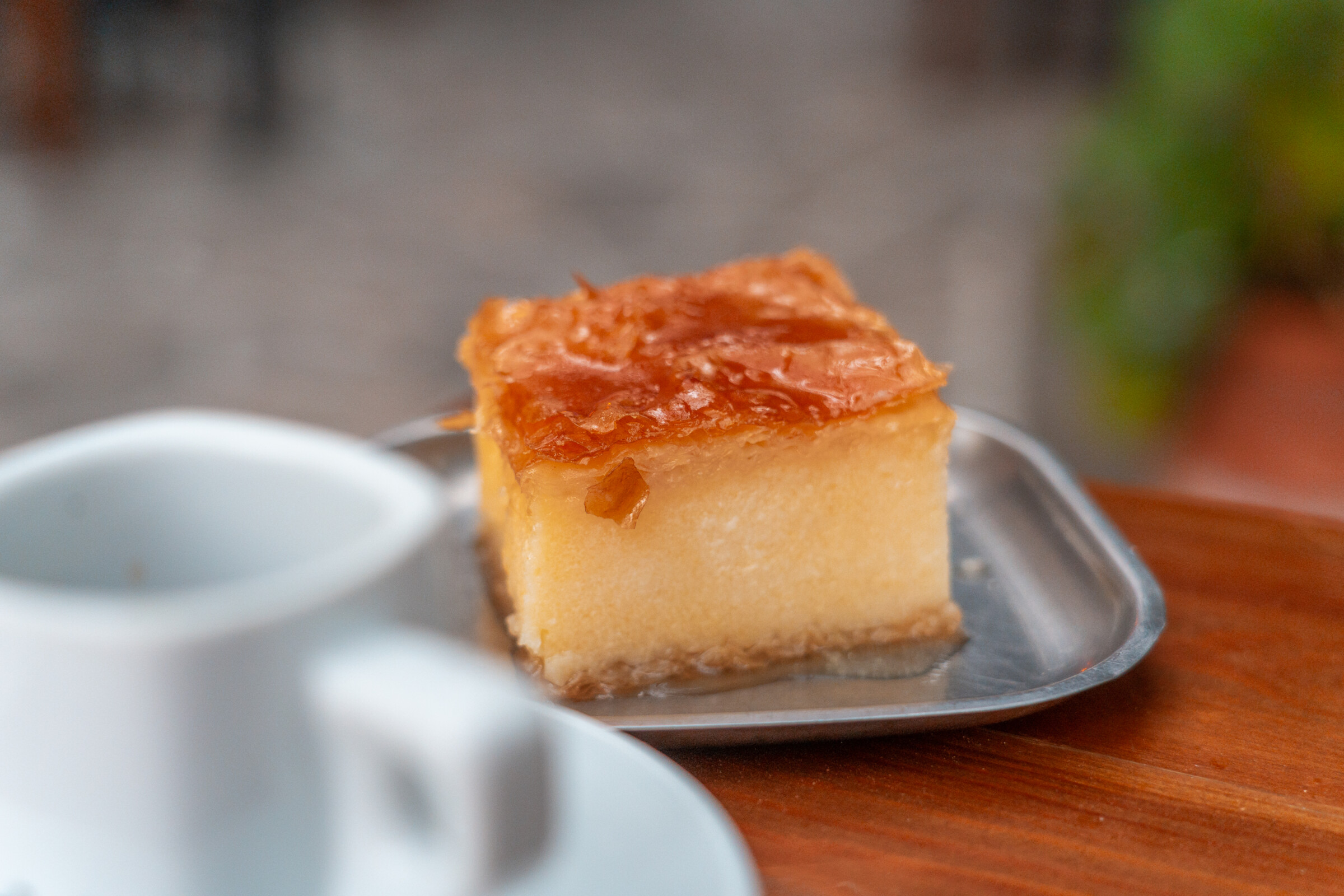 A piece of Galaktoboureko with a cup of Greek coffee in the foreground. 