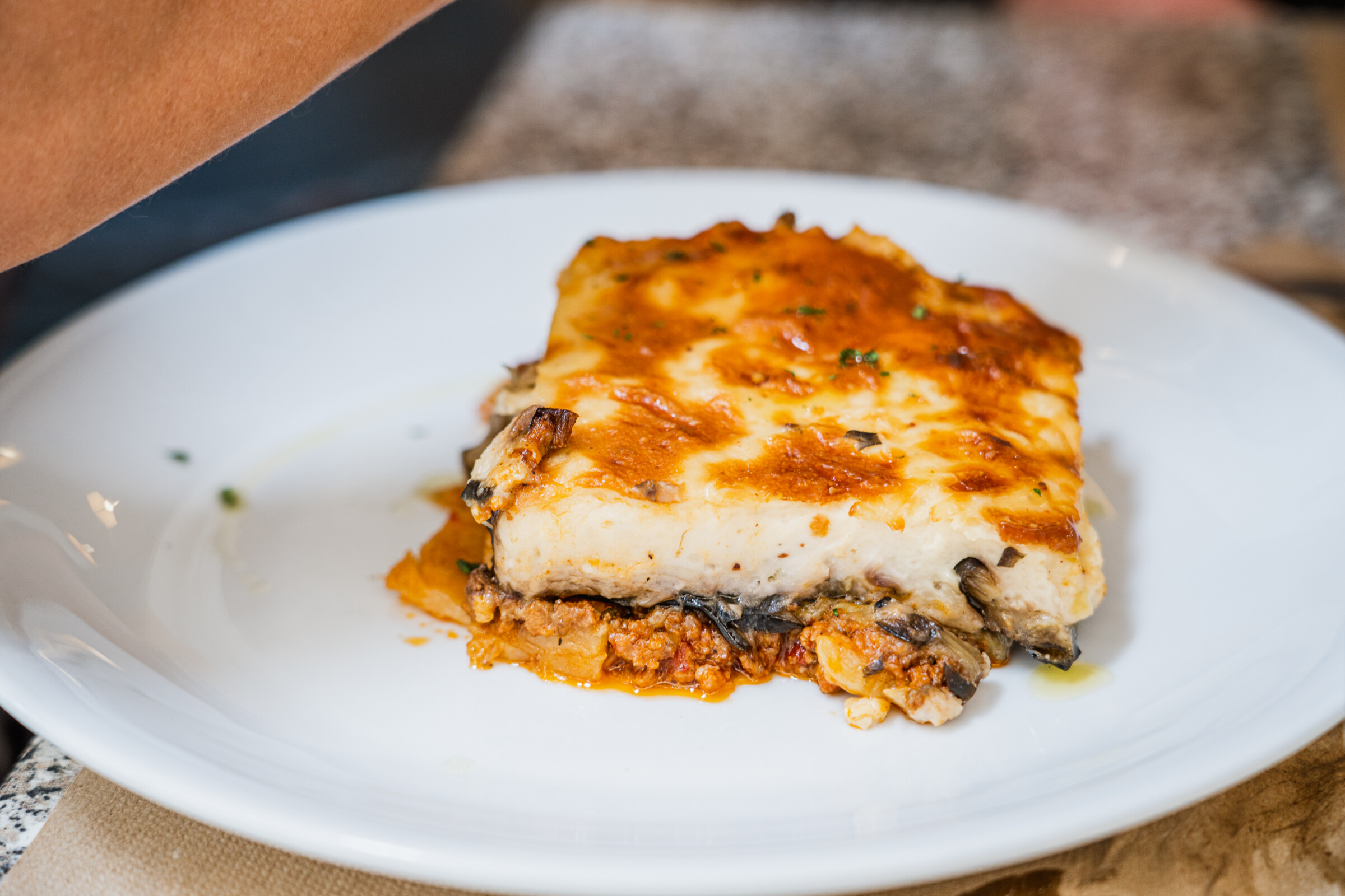 A close up of a white plate with a piece of Moussaka on it. 