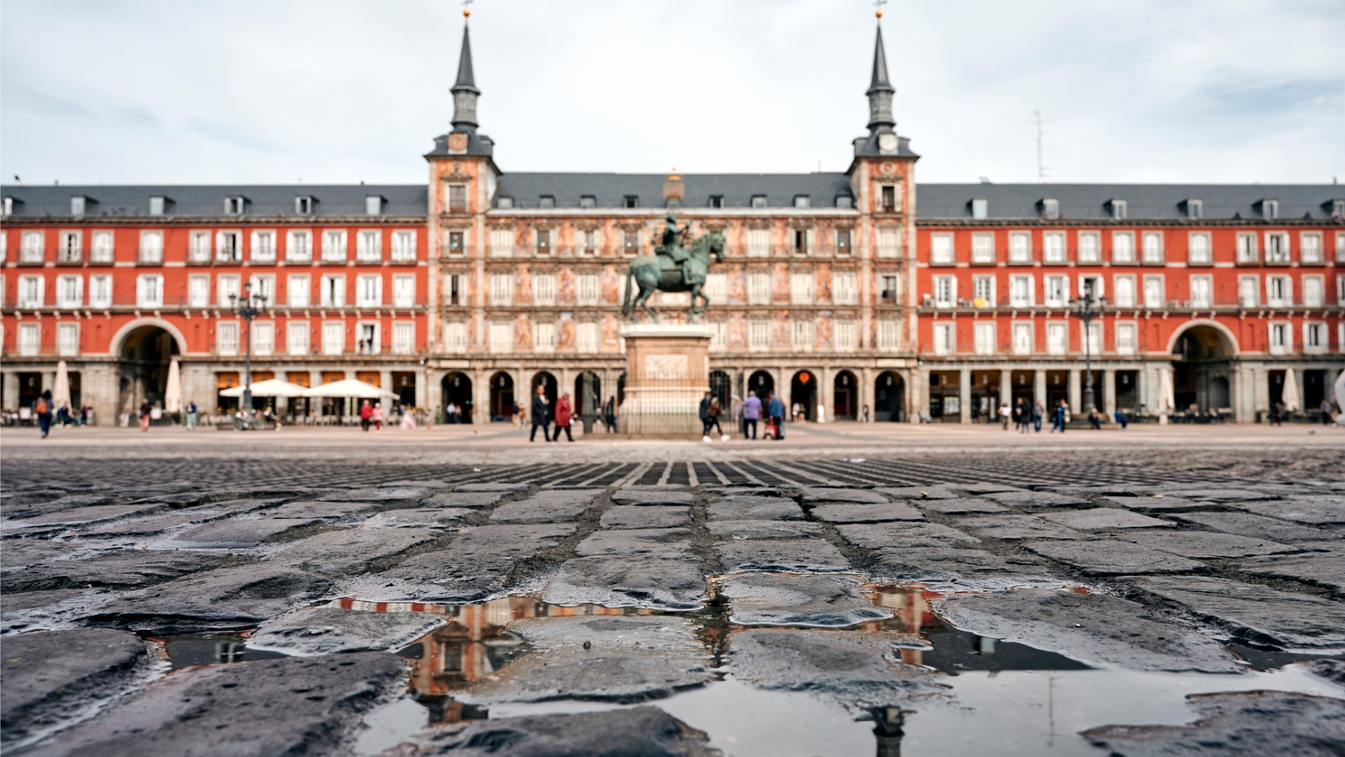 An image of Madrid's Plaza Mayor with puddles of rain water in the foreground. 