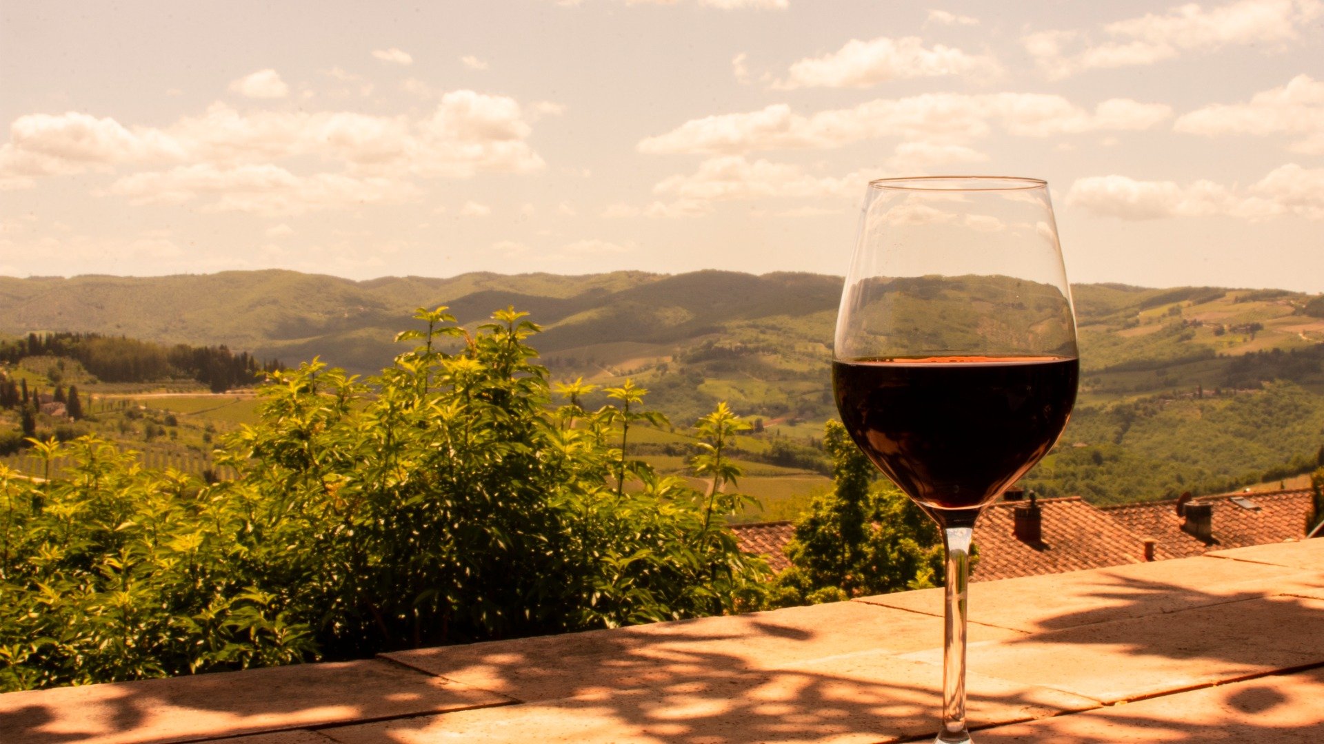 A glass of red wine in the foreground with the rolling hills of Tuscany in the background. 