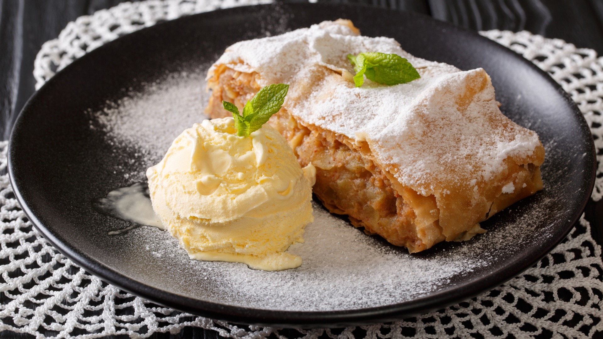 A slice of Apfelstrudel served with vanilla ice cream on the side and topped with icing sugar. 