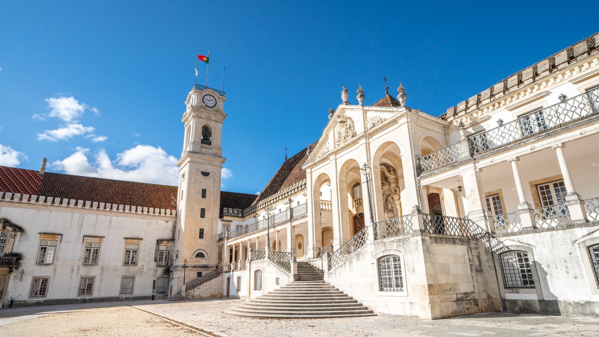 Tha facade of Coimbra University and a clock tower with the flag of Portugal on its top. 