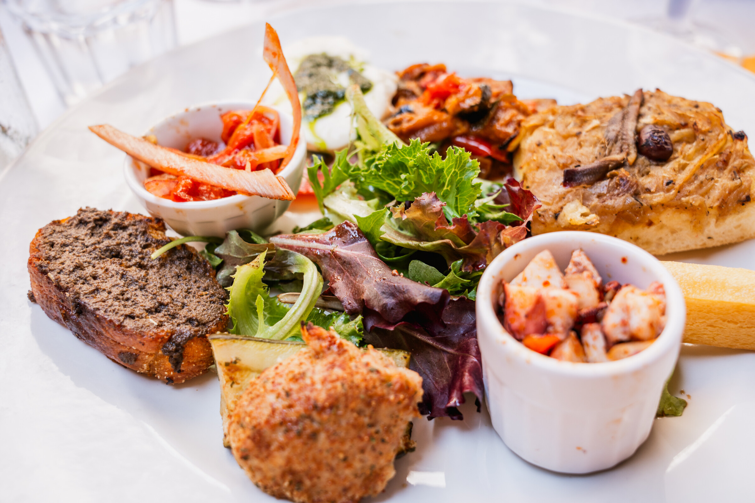 A close-up of a plate filled with small bites of several French delicacies. 