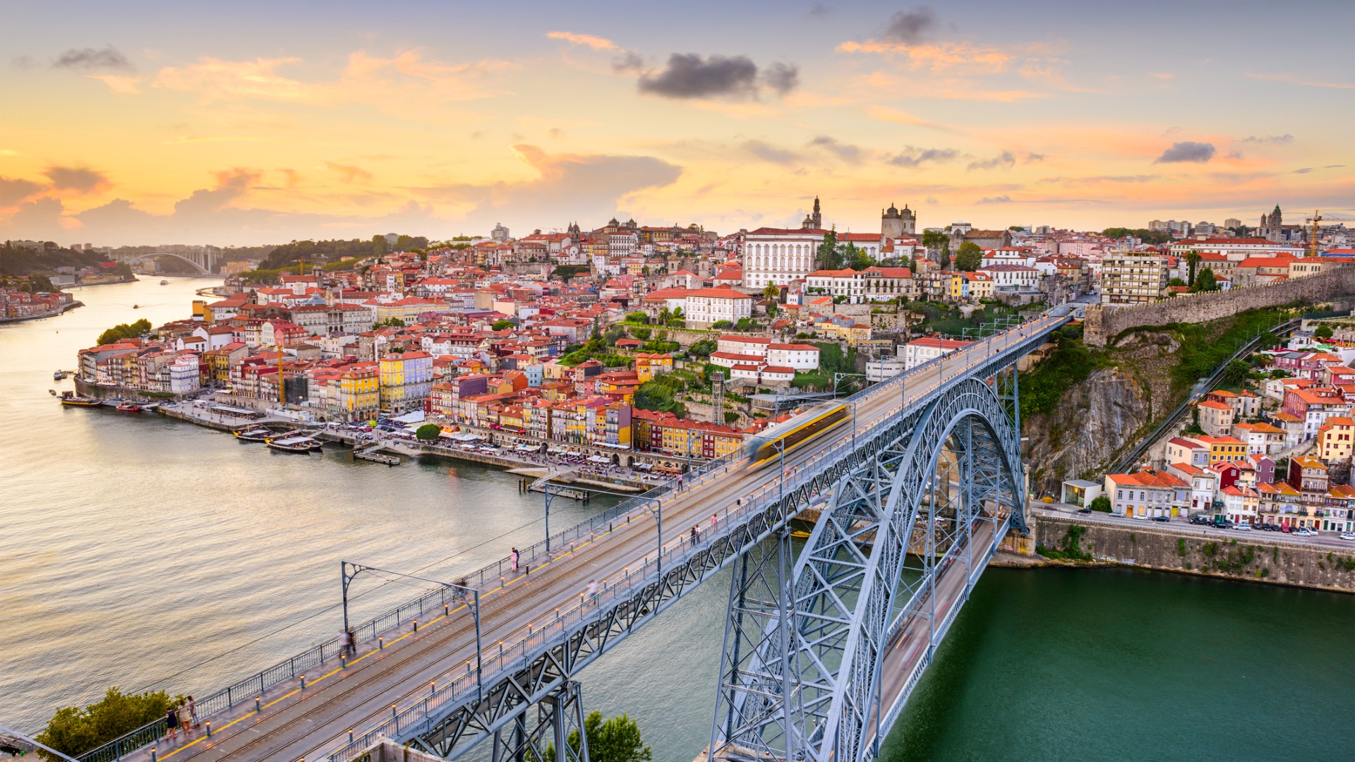 A panoramic view of Porto at sunset with the Luis I Bridge in the foreground.