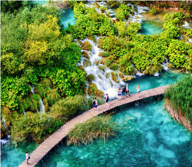 View of walkway in Plitvice Lakes, with bright turquoise water and vivid green trees.