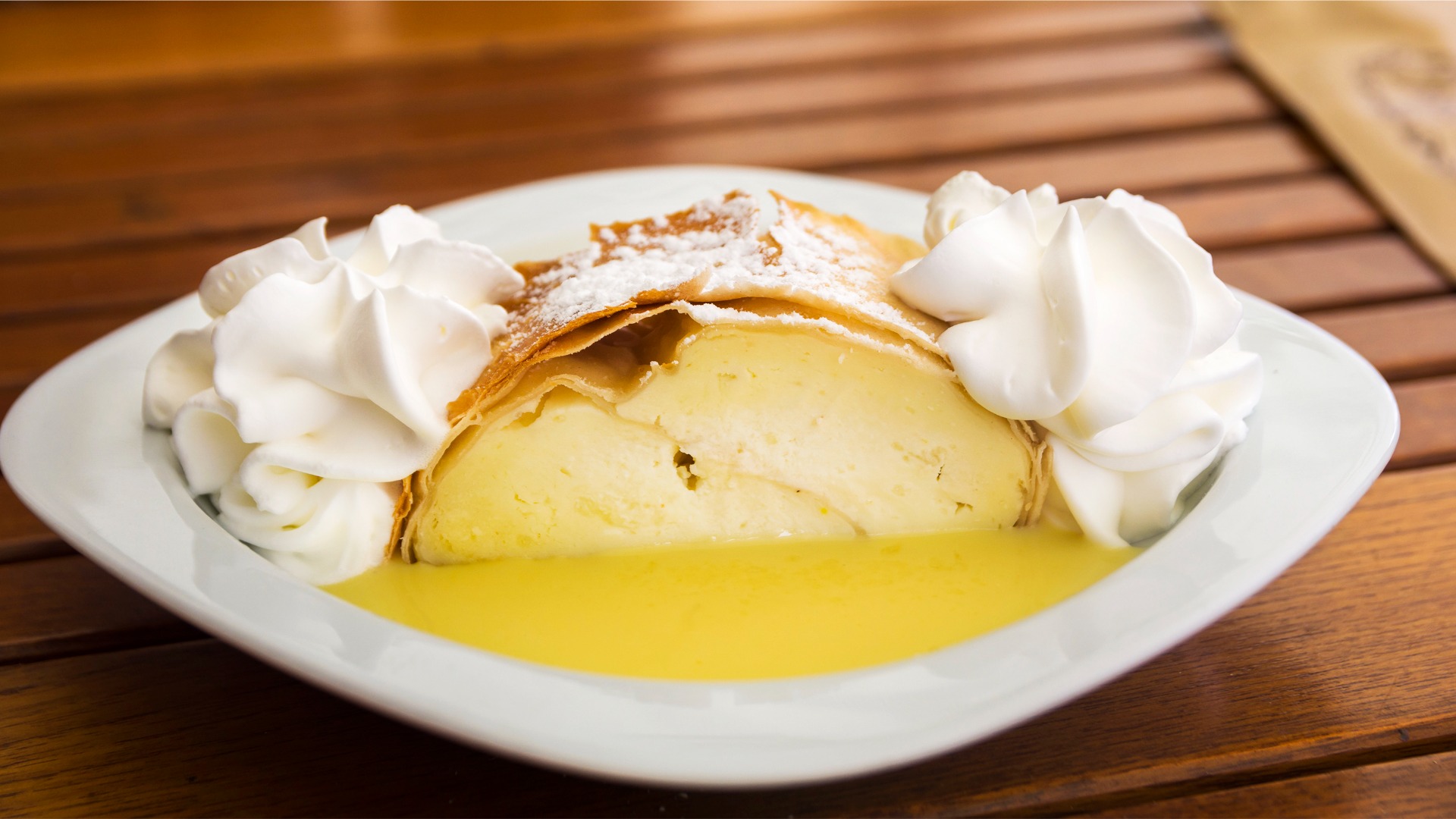 A close-up of Topfenstrudel with whipped cream and vanilla sauce on a wooden table. 