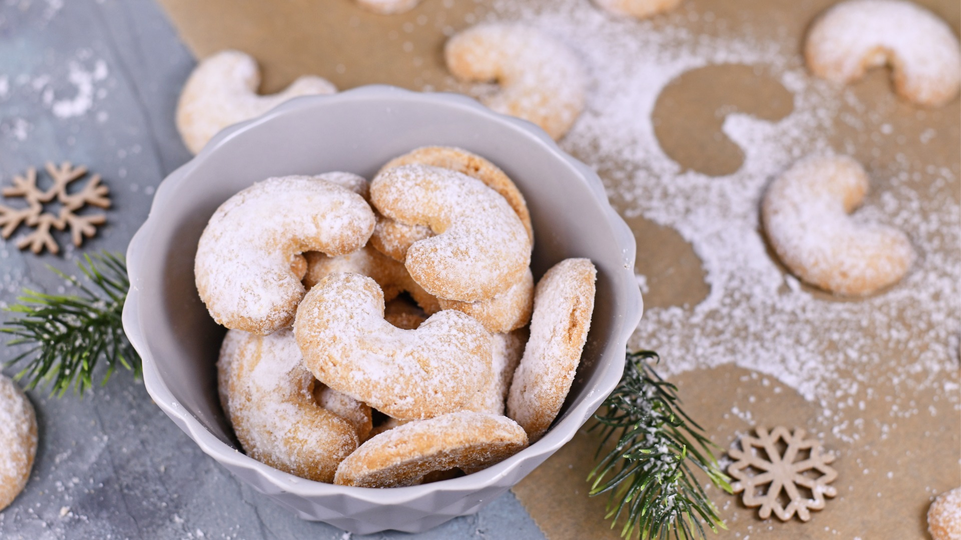 A bowl of crescent-shaped cookies sprinkled with icing sugar. 