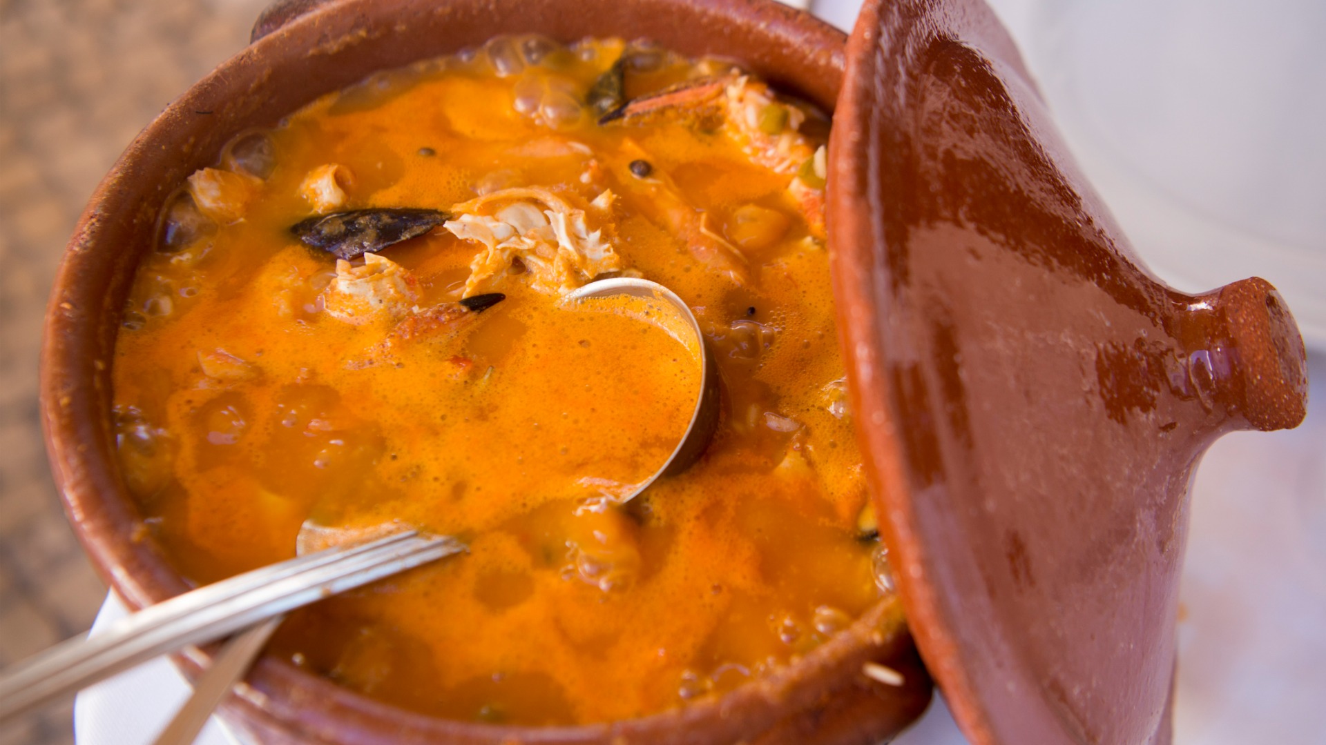 This image shows a clay pot filled with seafood rice in a tomato sauce. 