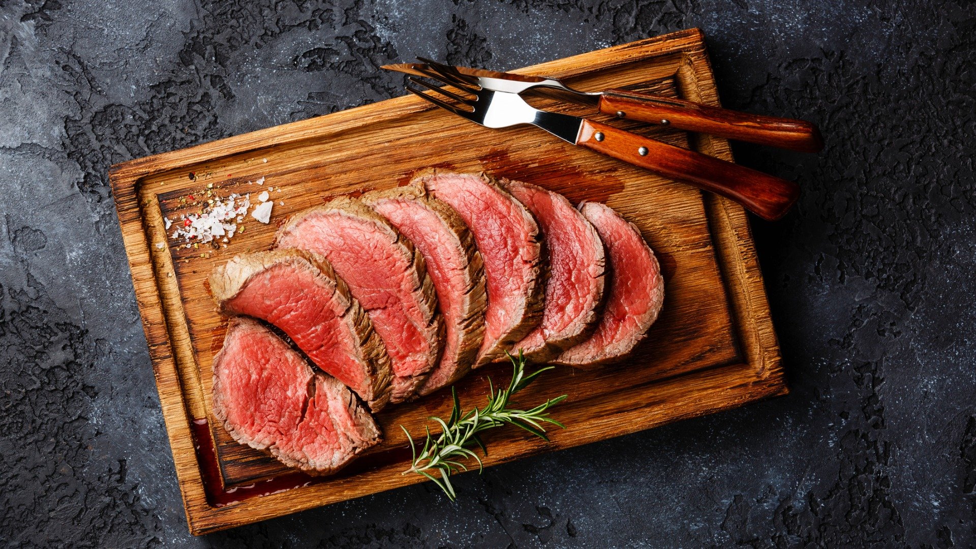 Sliced grilled tenderloin steak on a wooden cutting board.

