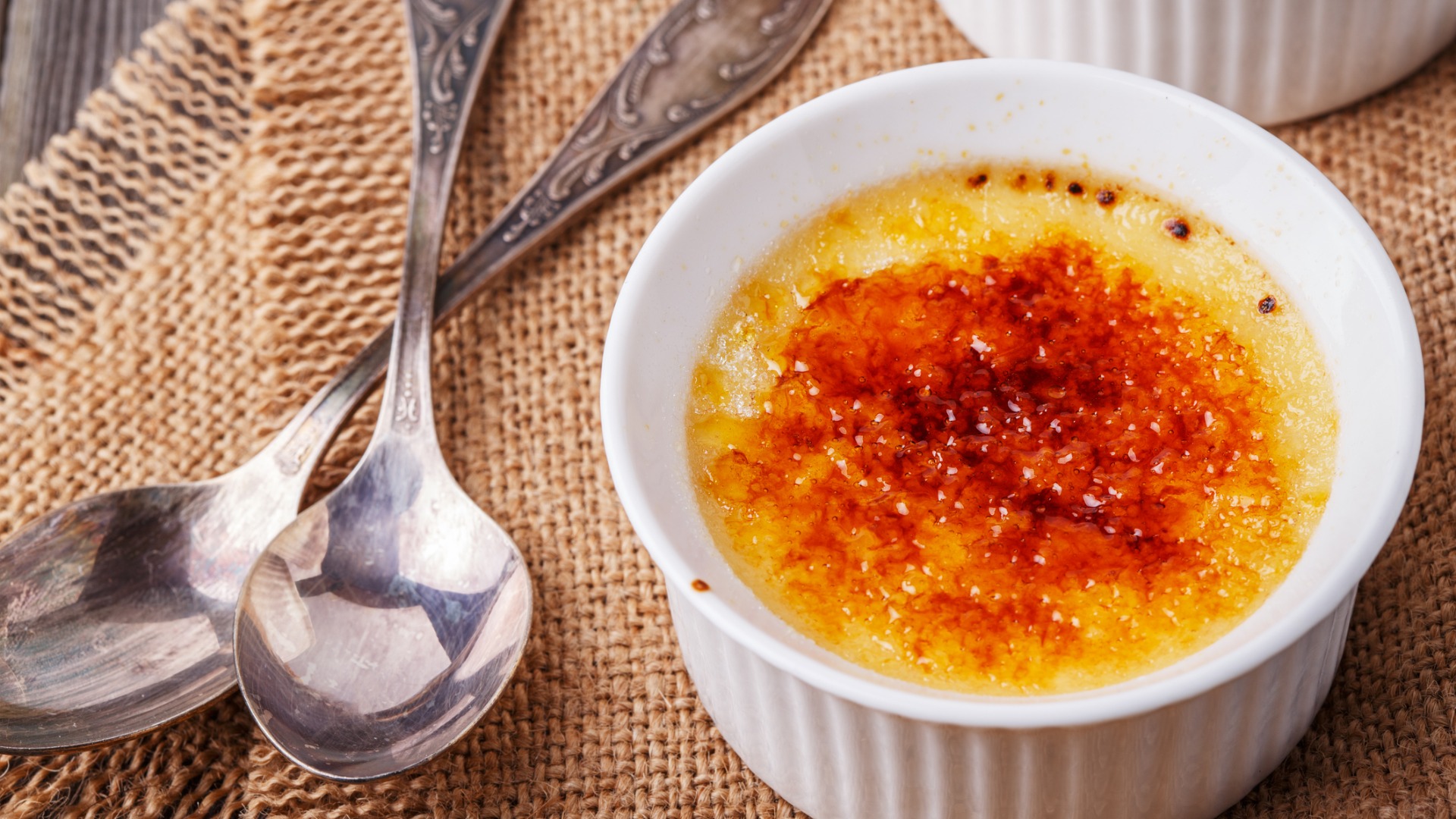 A close up of a bowl with Crème Brûlée and two spoons. 