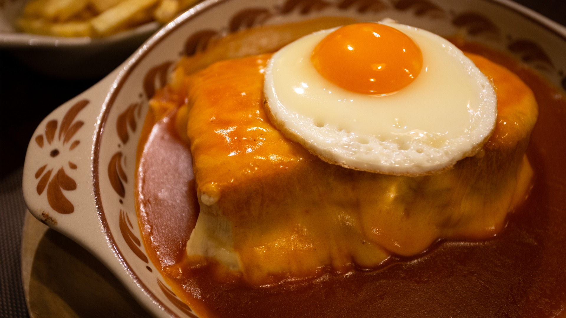 A close up of a Francesinha sandwich doused in a red sauce and topped with a fried egg. 