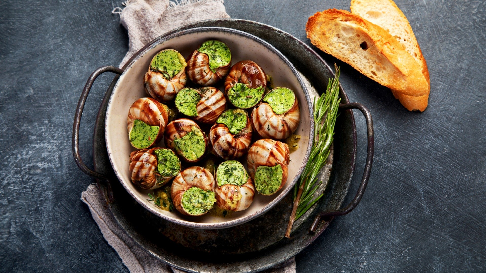 Snails with herbs and butter served with two slices of baguette bread. 