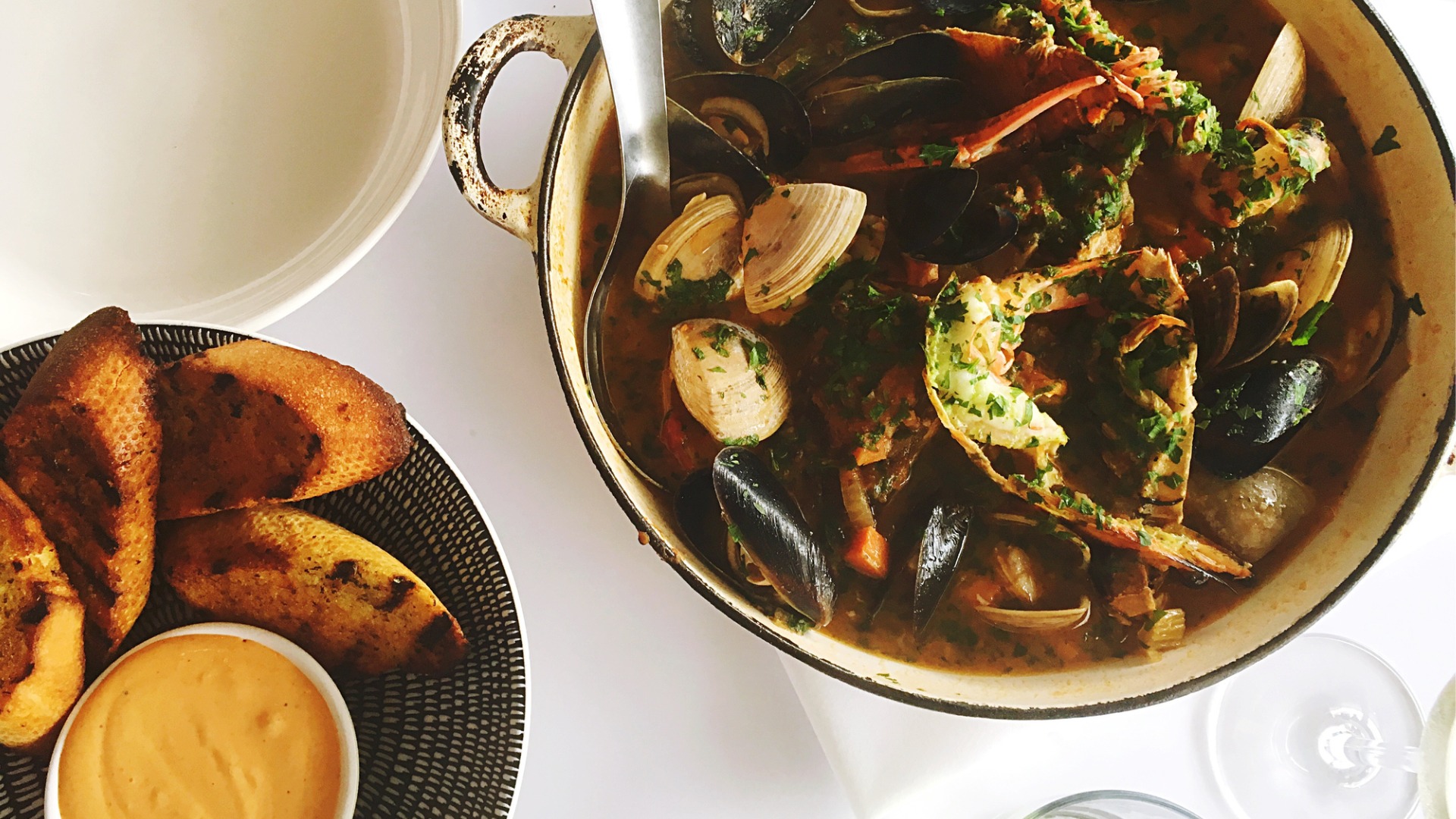 A close up of a bowl filled with French fish soup. Next to it, a smaller plate with toasted bread and a yellow sauce.