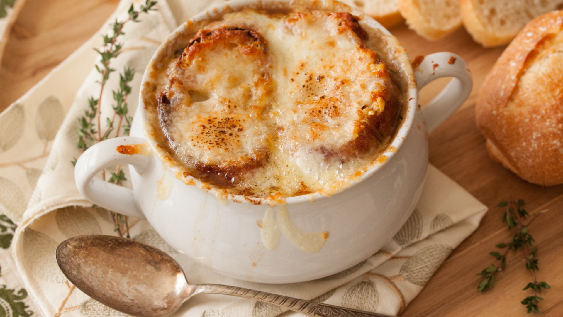 A close up of a bowl filled with French onion soup and two slices of bread with melted cheese on top. 