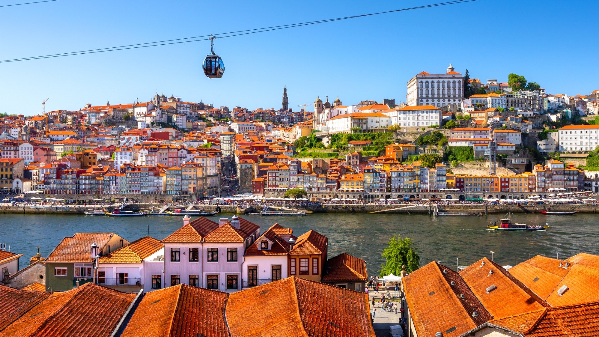 A panoramic view of Porto's red-rooftoped buildings with the cable car above. 