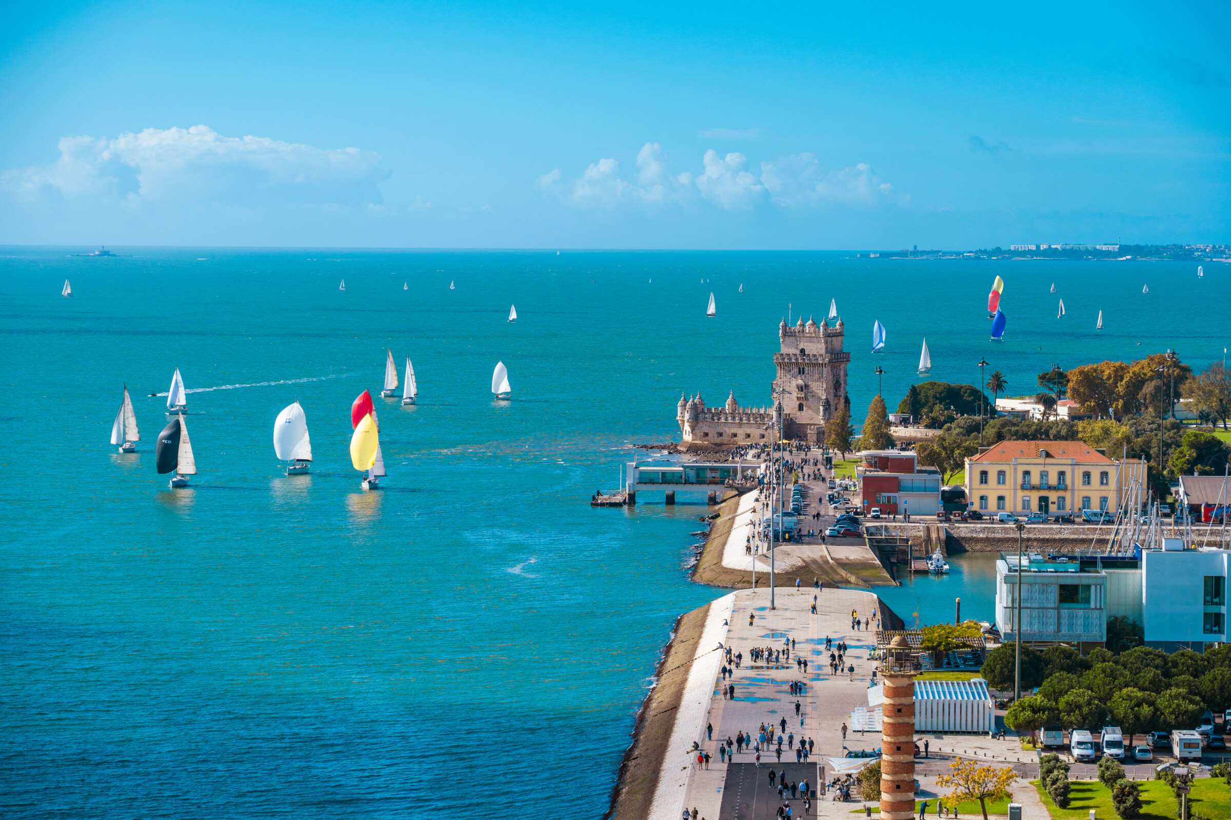 A panoramic view of Belem Tower, the Tagus River, and the promenade on a sunny day. 