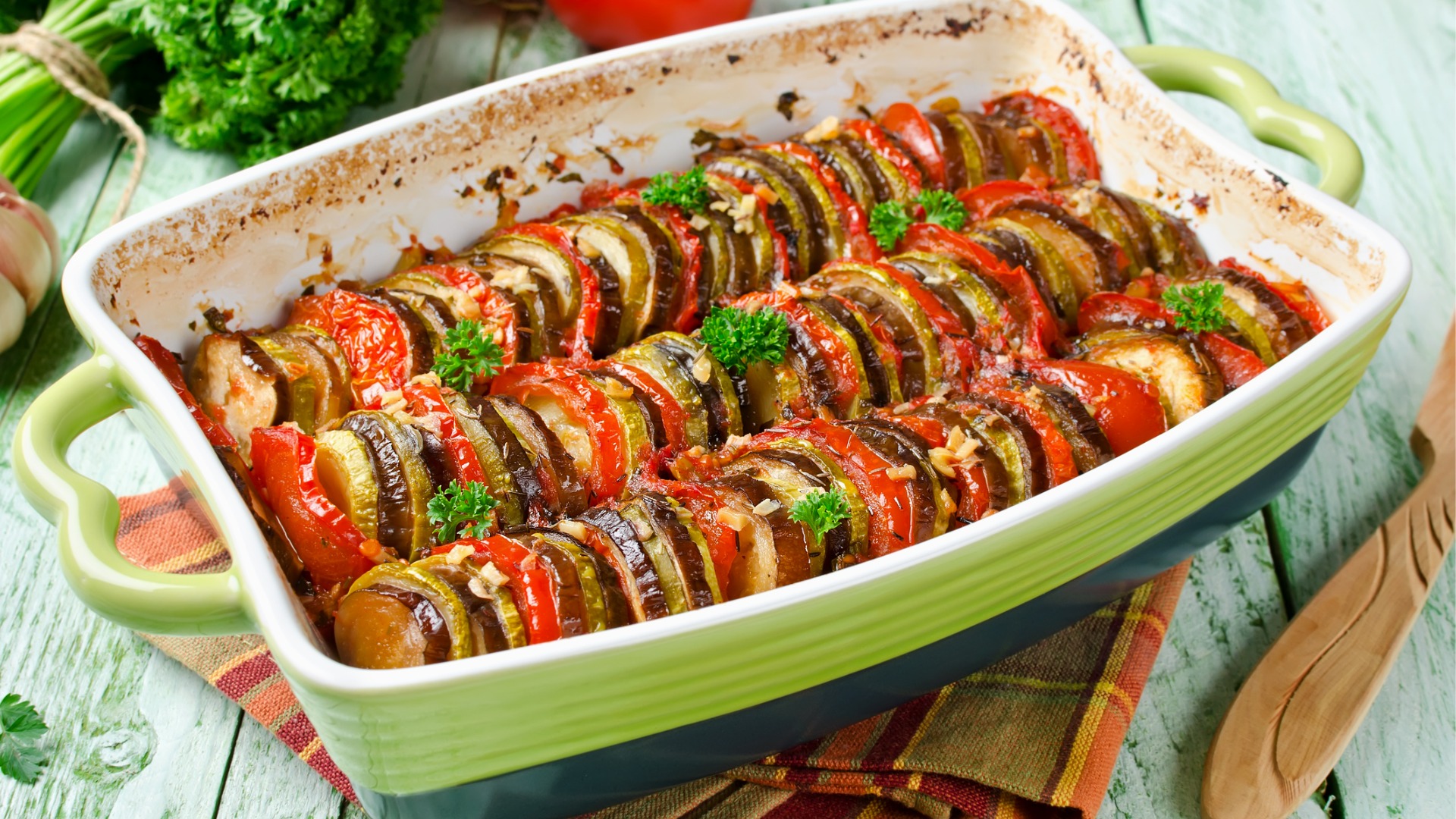 A light-green ceramic baking dish with rows of vegetables: green bell peppers, eggplant, and zucchini. 