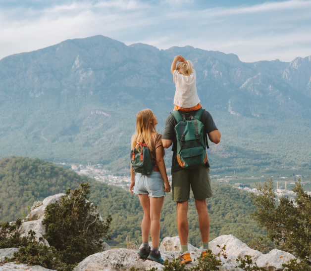 A couple and their child, sitting on the father's shoulders, looking at a mountain panorama.