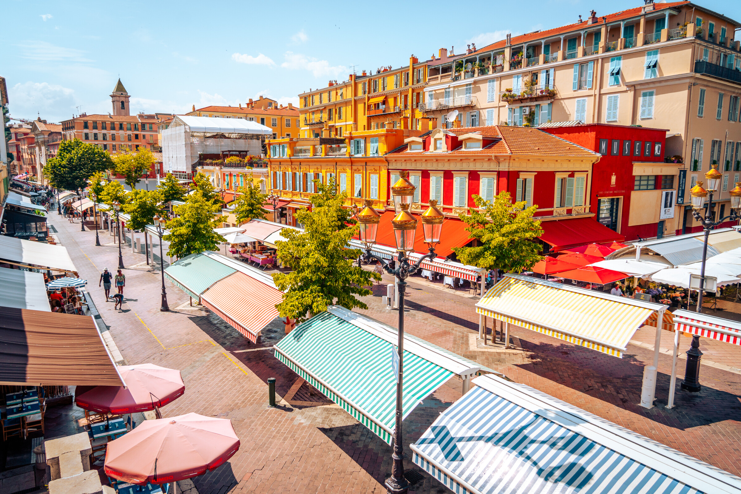 A pedestrianised street lined with beautiful colourful buildings, cafés and restaurants. Two people are walking along the street. 