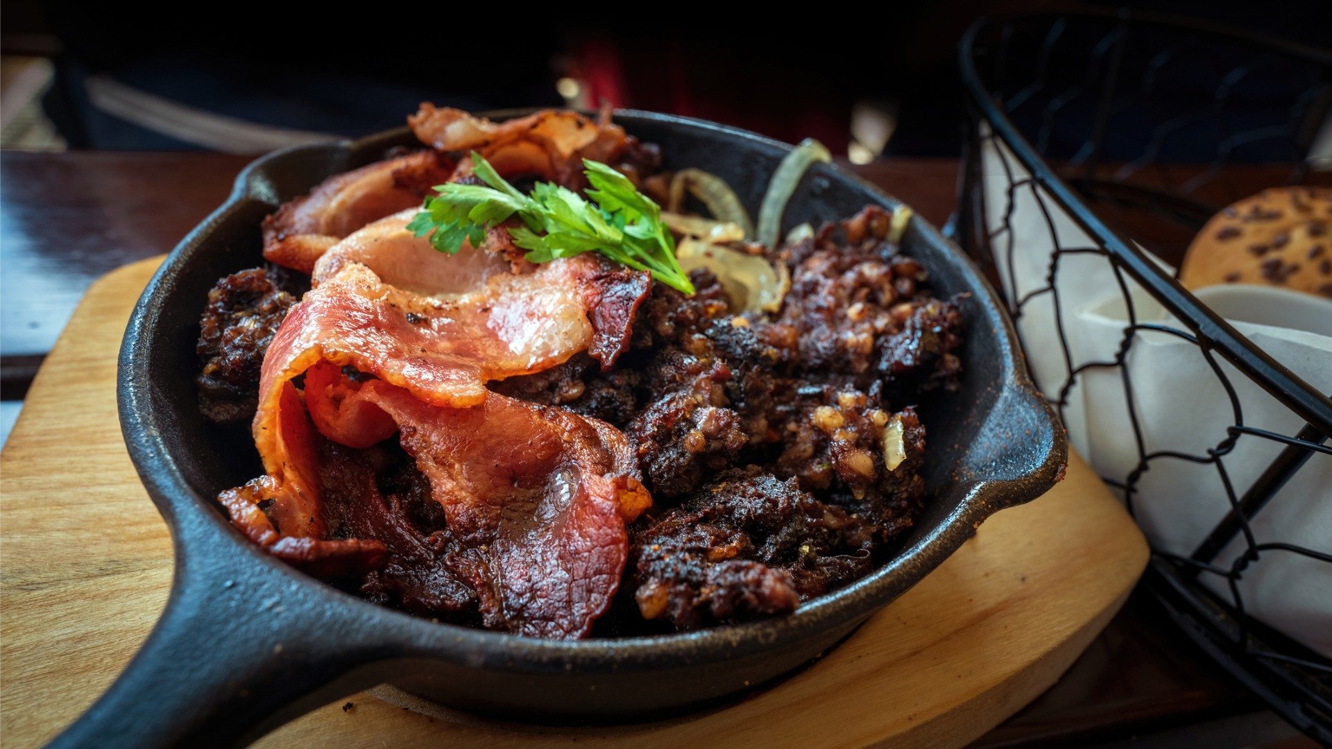 A cast-iron skillet with pieces of blood sausage and bacon slices. 