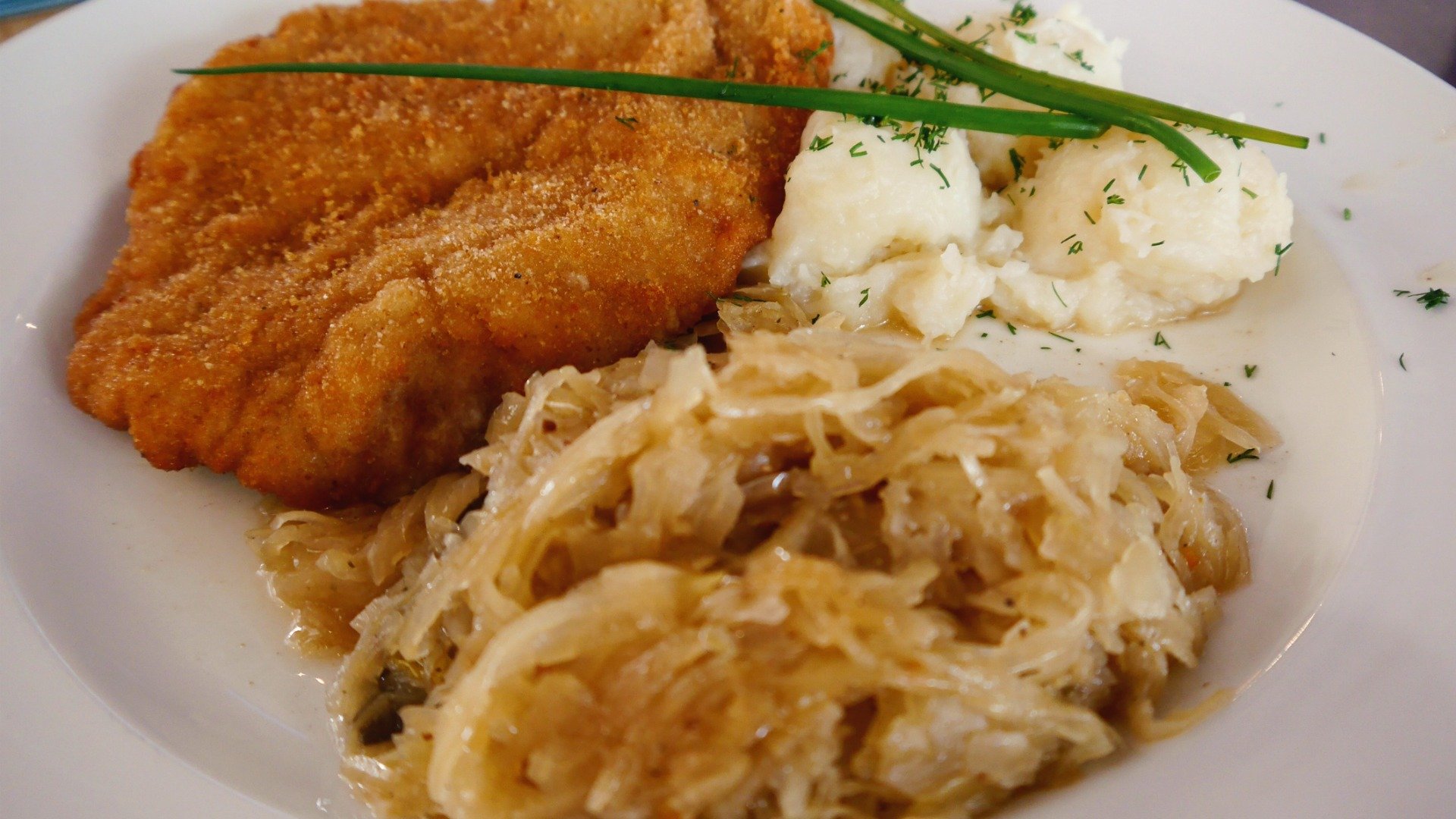 A white plate with a pork Schnitzel, cabbage, and mashed potatoes. 