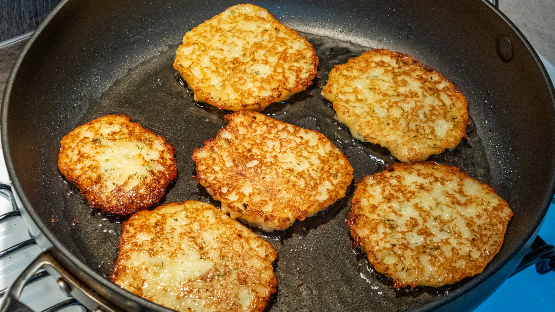 A frying pan with six potato pancakes. 