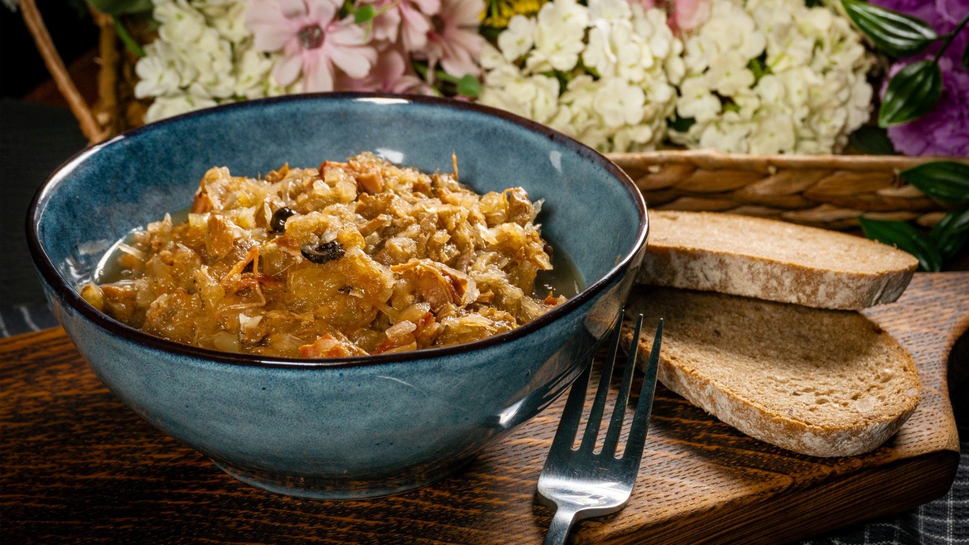 A blue bowl filled with meat soup served with slices of rye bread on the side. 