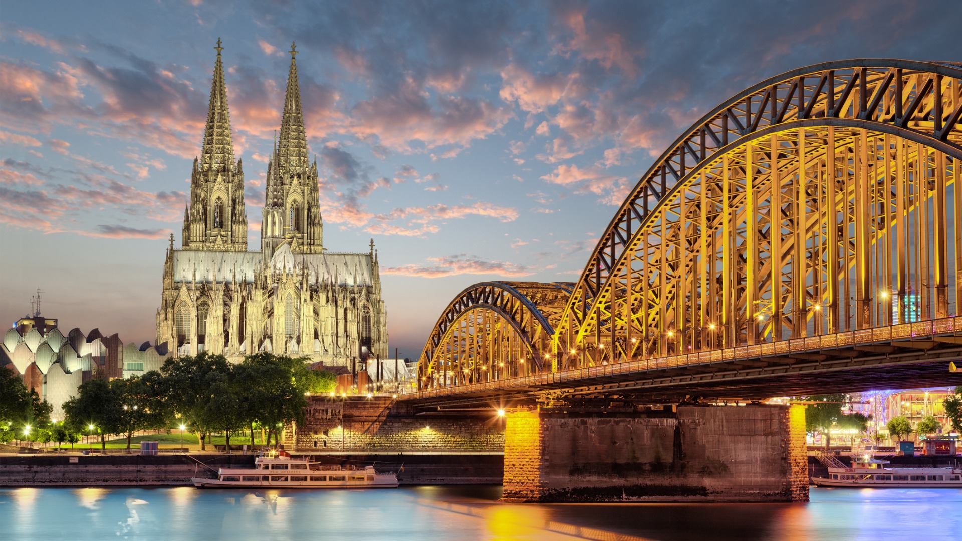 An imposing Cathedral under a blue sky with pink clouds, next to an impressive bridge. 