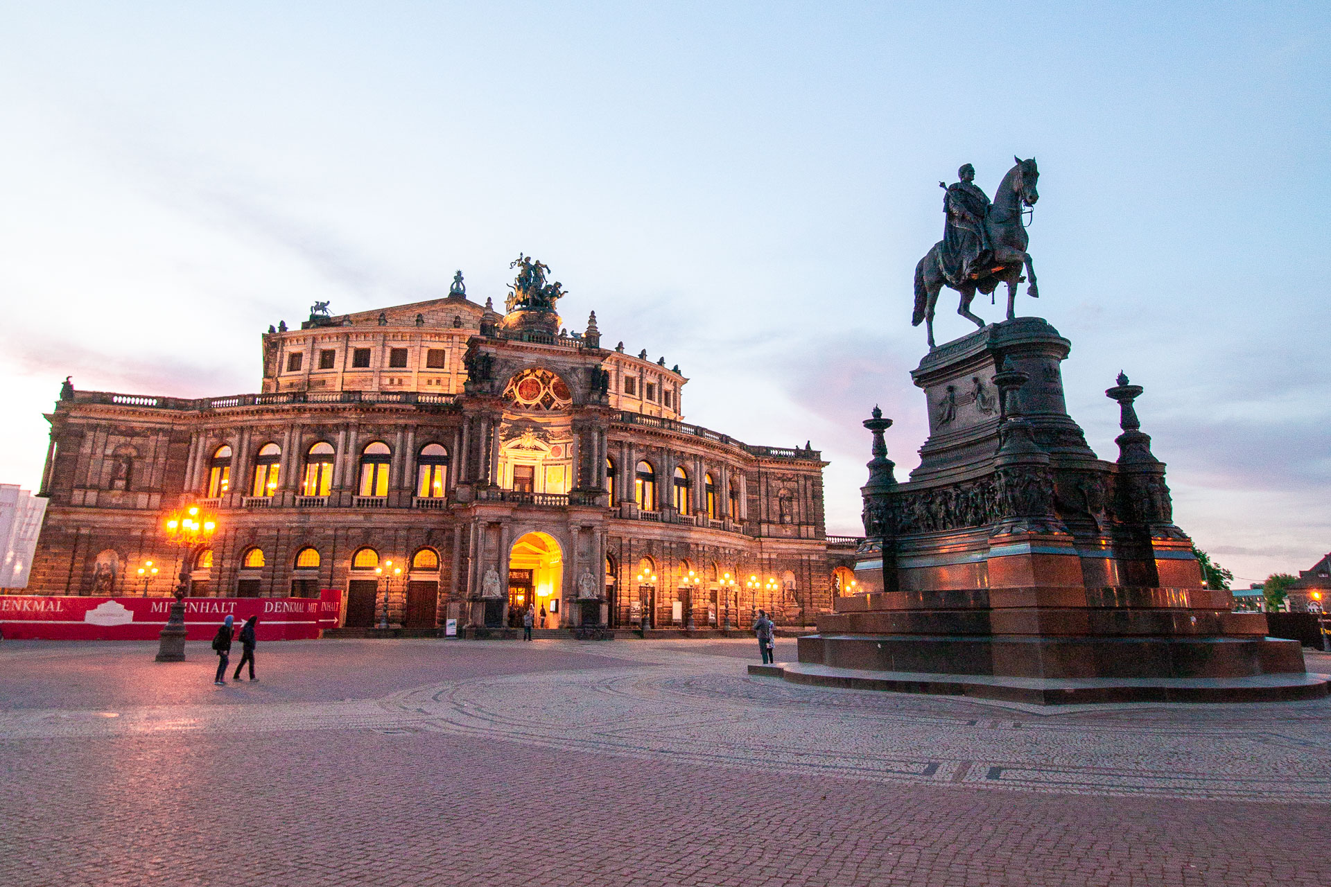 A beautifully lit building and a large statue of a man riding a horse on a quiet square. 