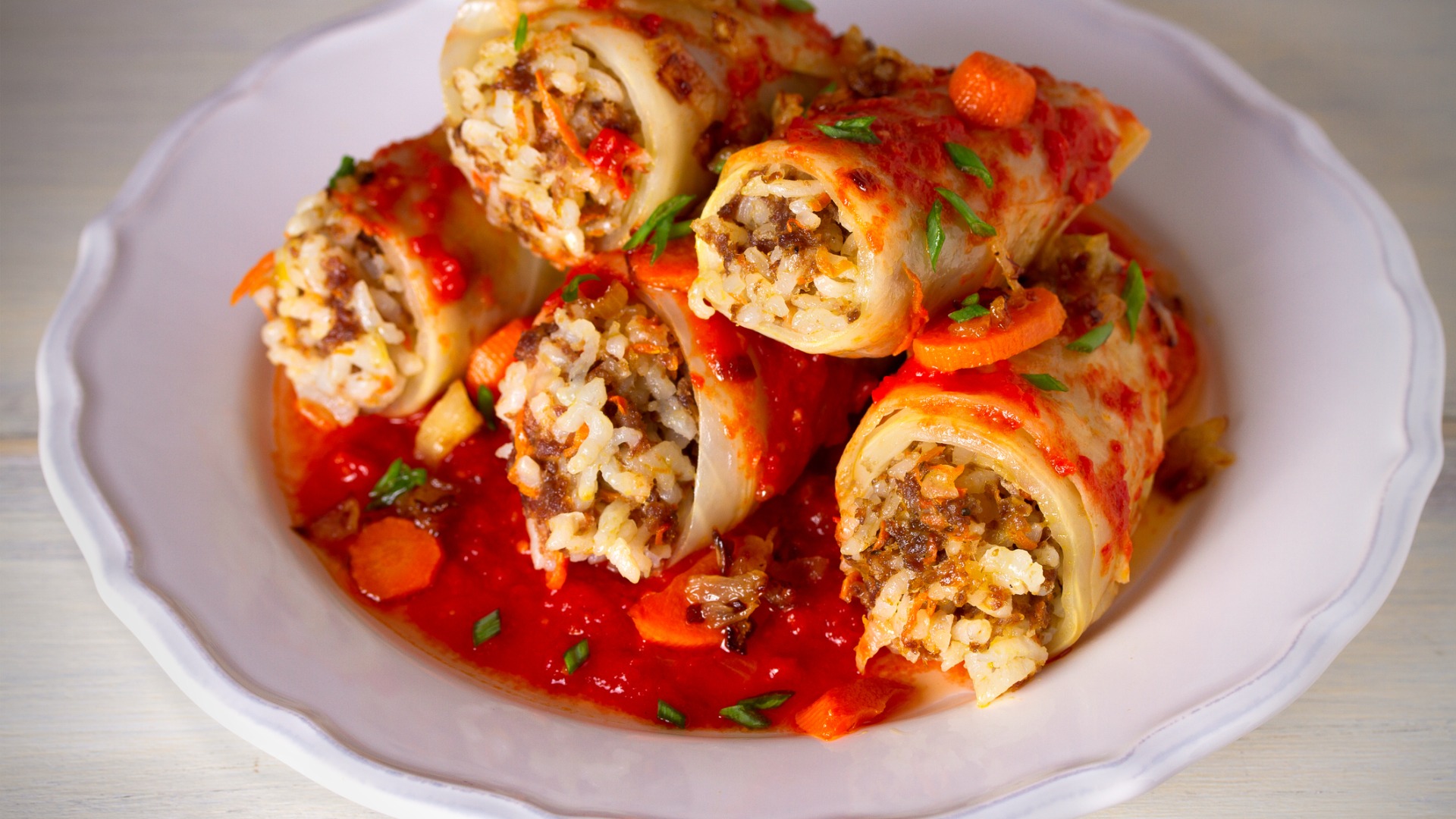 A white plate filled with stuffed cabbage leaves. 