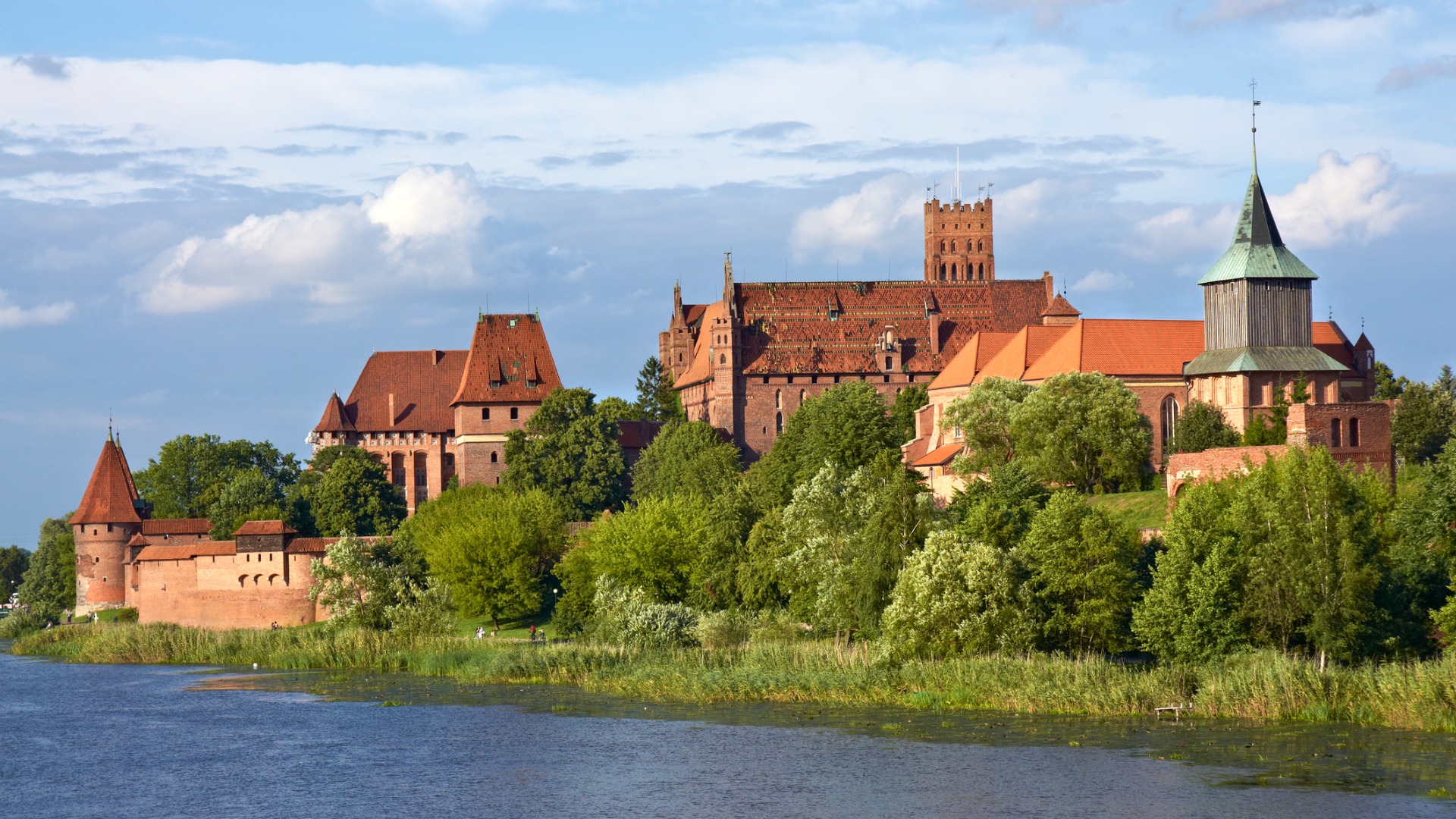 A castle built along a river amidst lush greenery. 