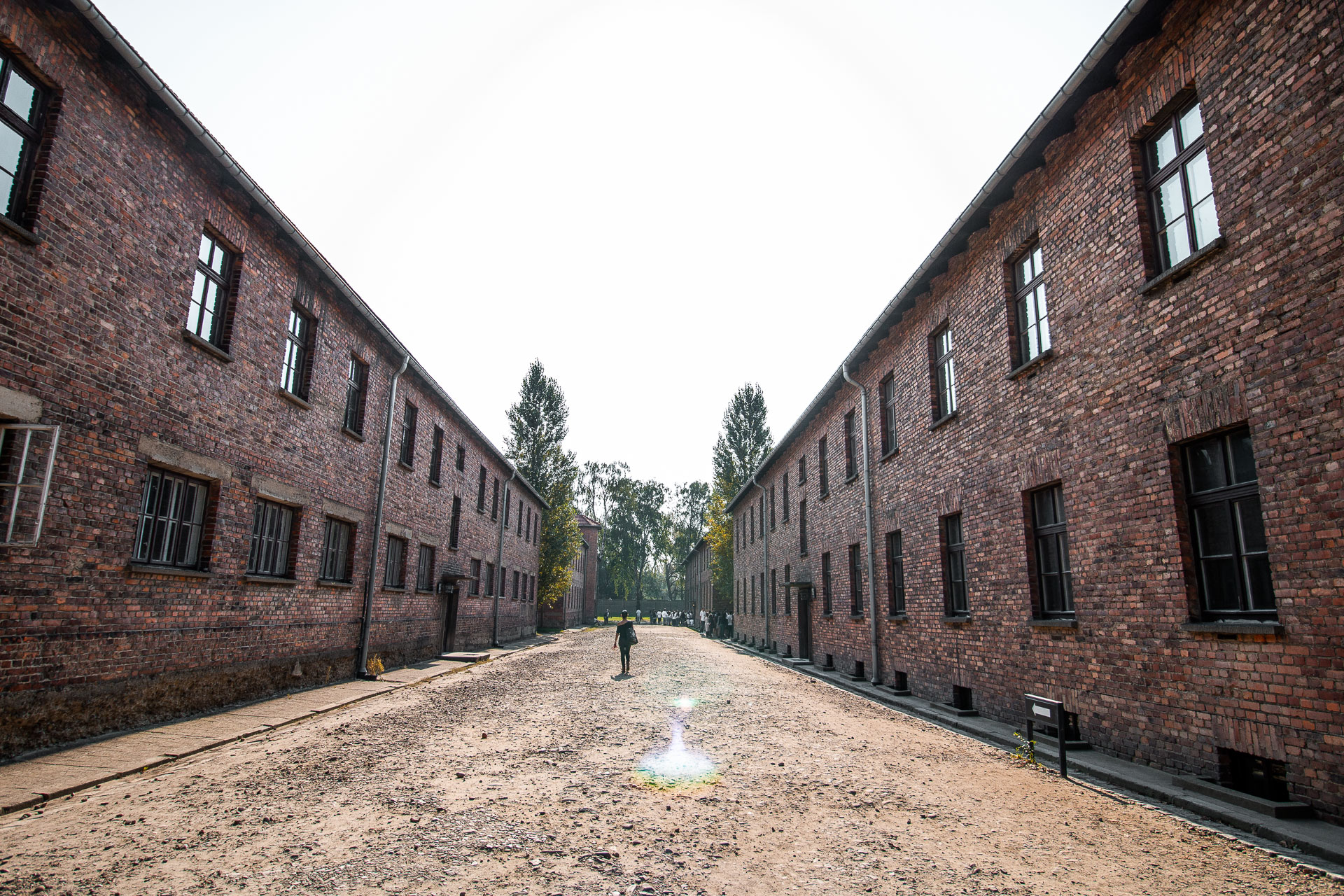 A woman walking on a dirt street. A brick building lines either side of the street.  