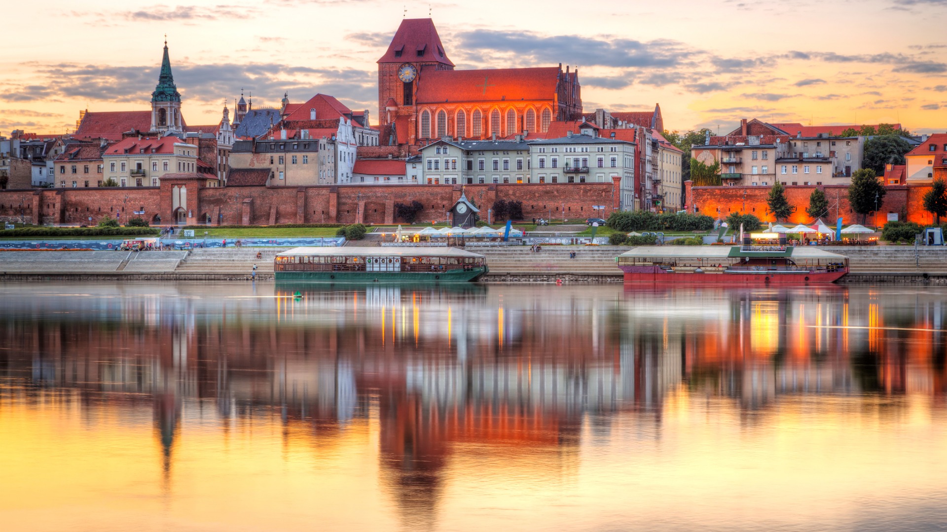 A beautiful Old Town under a sunset sky. Reflections of the buildings and the orange sky on the waters of the river. 