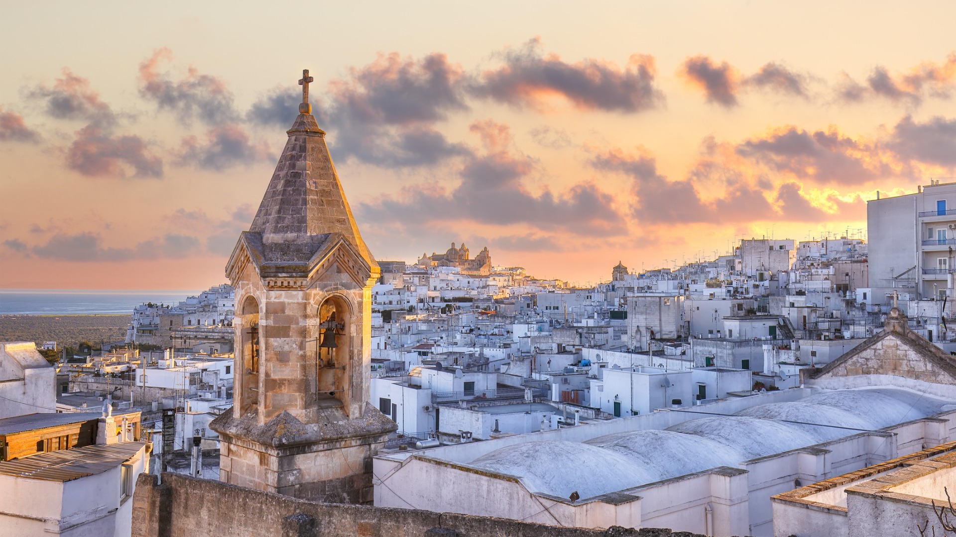 A panoramic view of whitewashed Ostuni at sunset with an old bell tower in the foreground. 