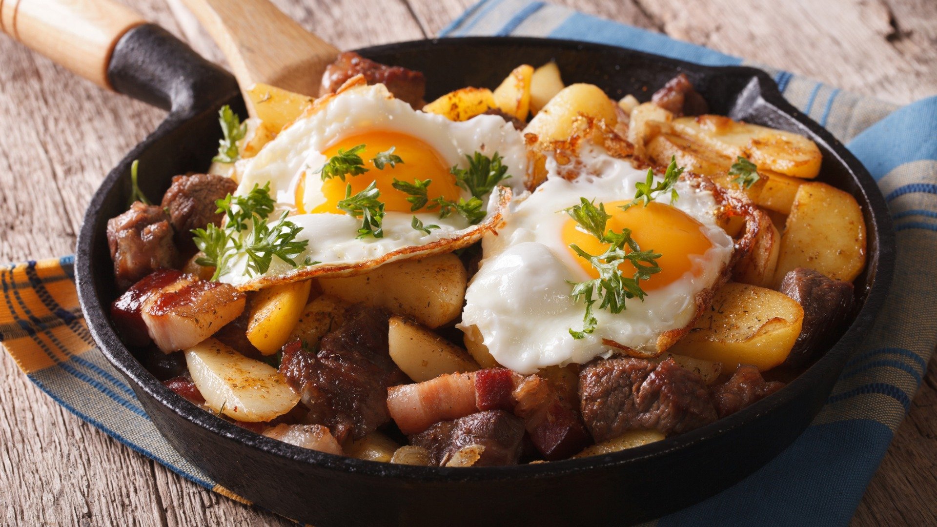 A cast-iron pan filled with fried potatoes and bacon and topped with two fried eggs. 