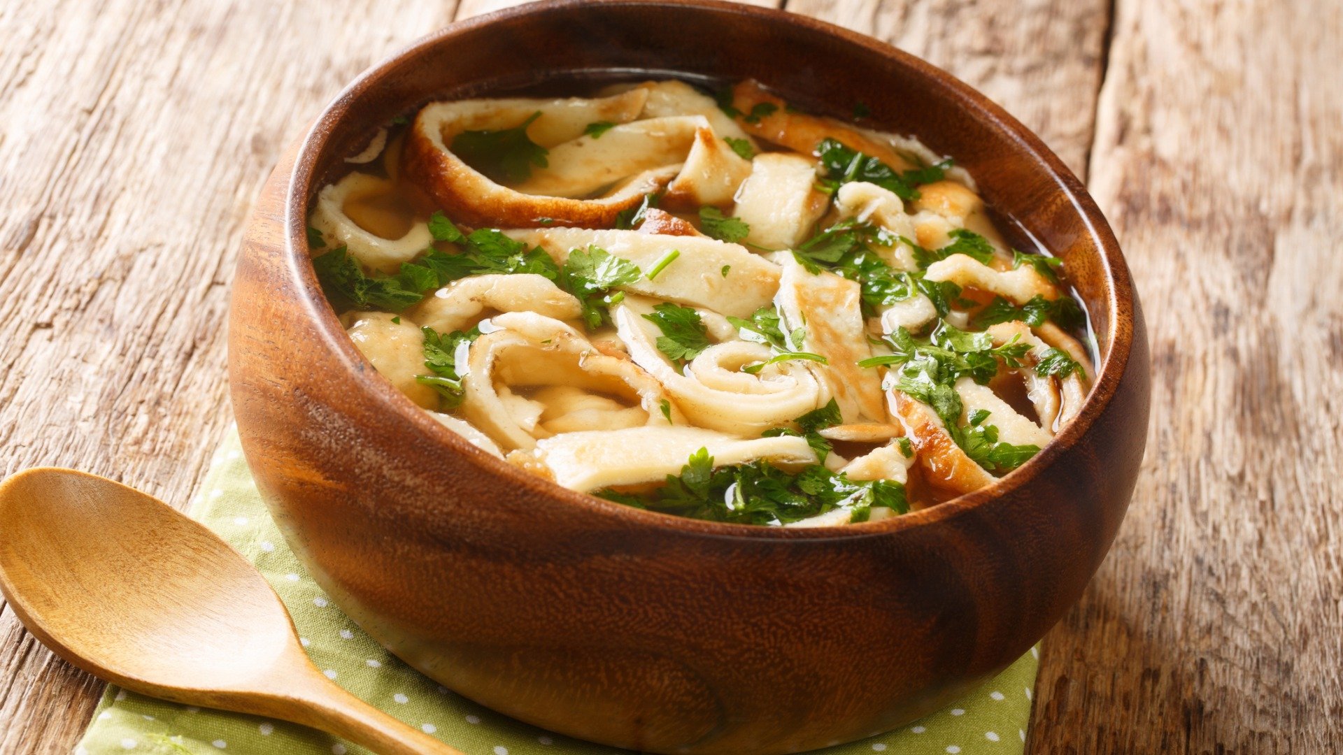 A wooden bowl filled with soup made of pancake strips and greens. Frittatensuppe is the best Austrian food for comfort. 