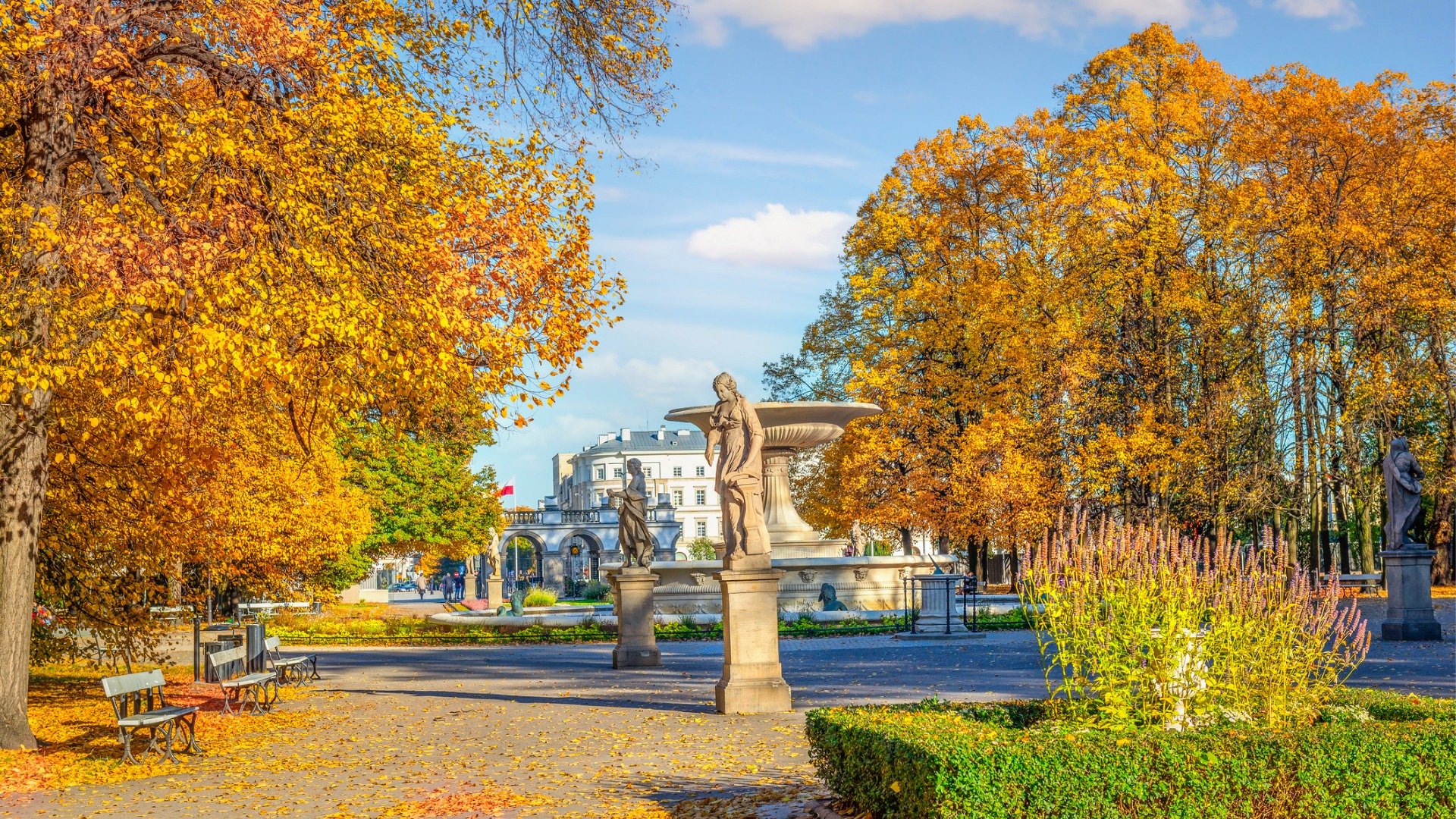 Statues and benches in a park where trees are adorned by gorgeous fall foliage. 