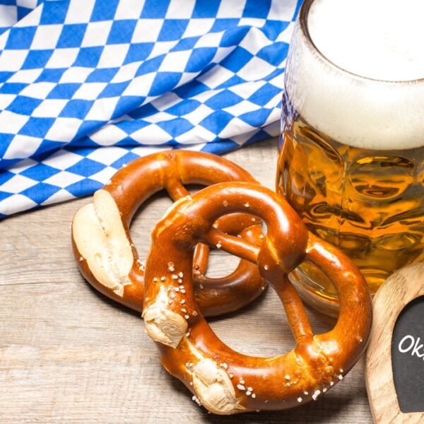 A mug of beer, two pretzels, a wooden heart that has Oktoberfest written on it, and a Bavarian flag in the background.