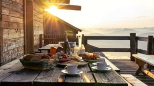 A breakfast table set on a rustic wooden terrace patio of a mountain hut in Tirol at sunrise.