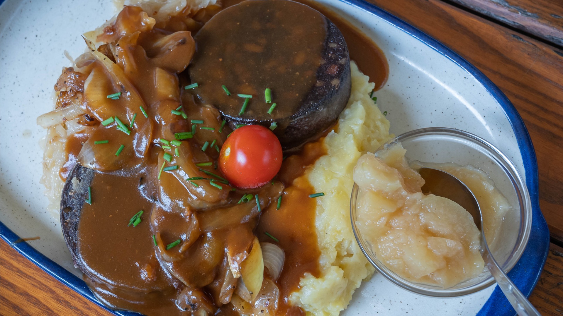 Mashed potatoes topped with blood sausage and an onion sauce. There's also apple puree in a small bowl.