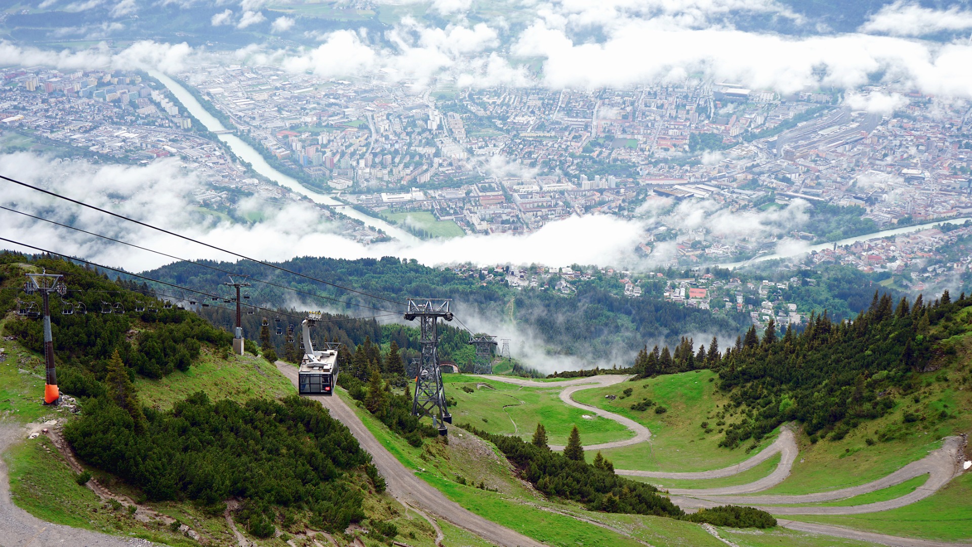 A panoramic view of a mountain slope with a cable car and Innsbruck in the background. 