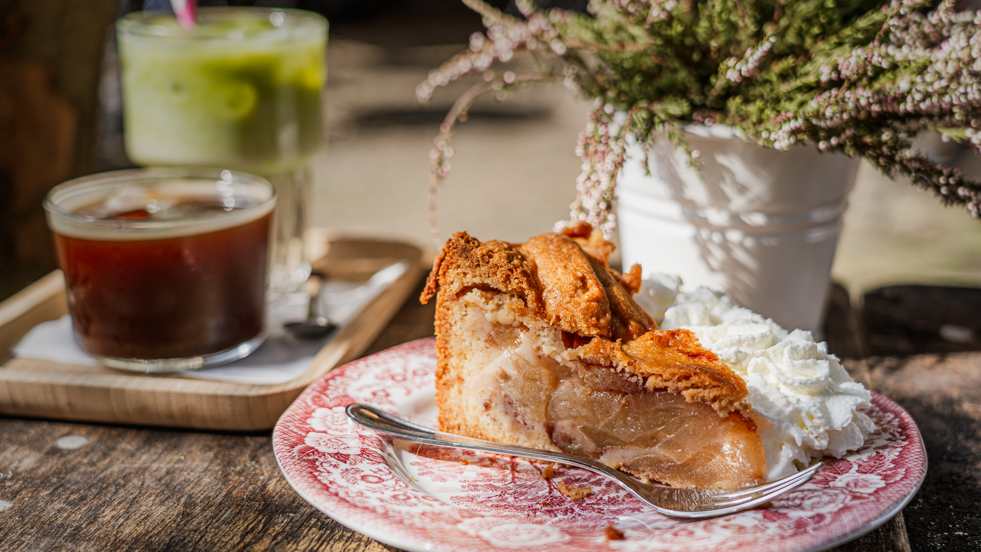 A slice of Dutch apple pie - appeltaart - on a porcelain plate surrounded by coffee and flowers.