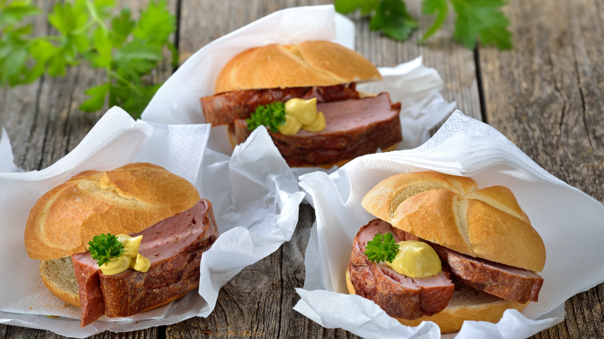 Three bread rolls filled with meatloaf and mustard. 