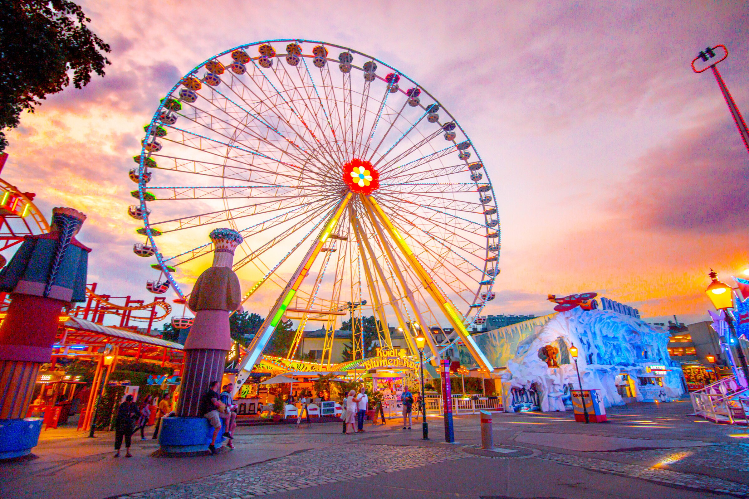 A Ferris Wheel at an amusement park under a pink and orange sunset sky. 