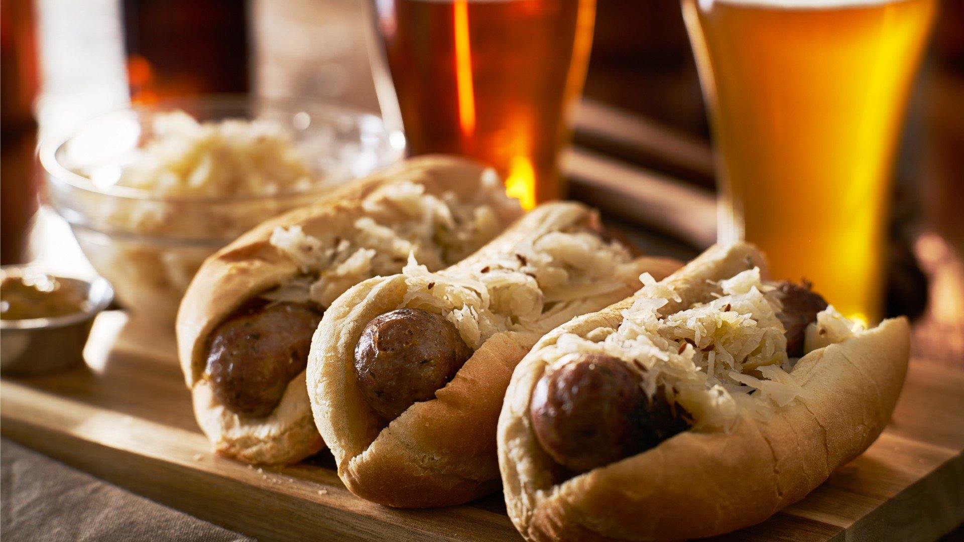 Three bread rolls filled with sausage and Sauerkraut, for many, the best German food. Two glasses of beer in the background. 