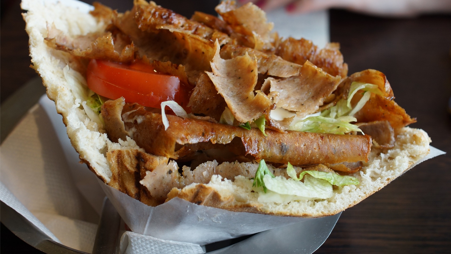 A close up of a pita bread with Doner Kebab, lettuce, and tomatoes. 