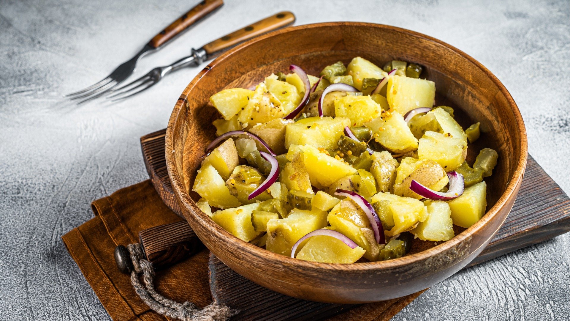 A wooden bowl with boiled potatoes, chopped pickles, and onions. 