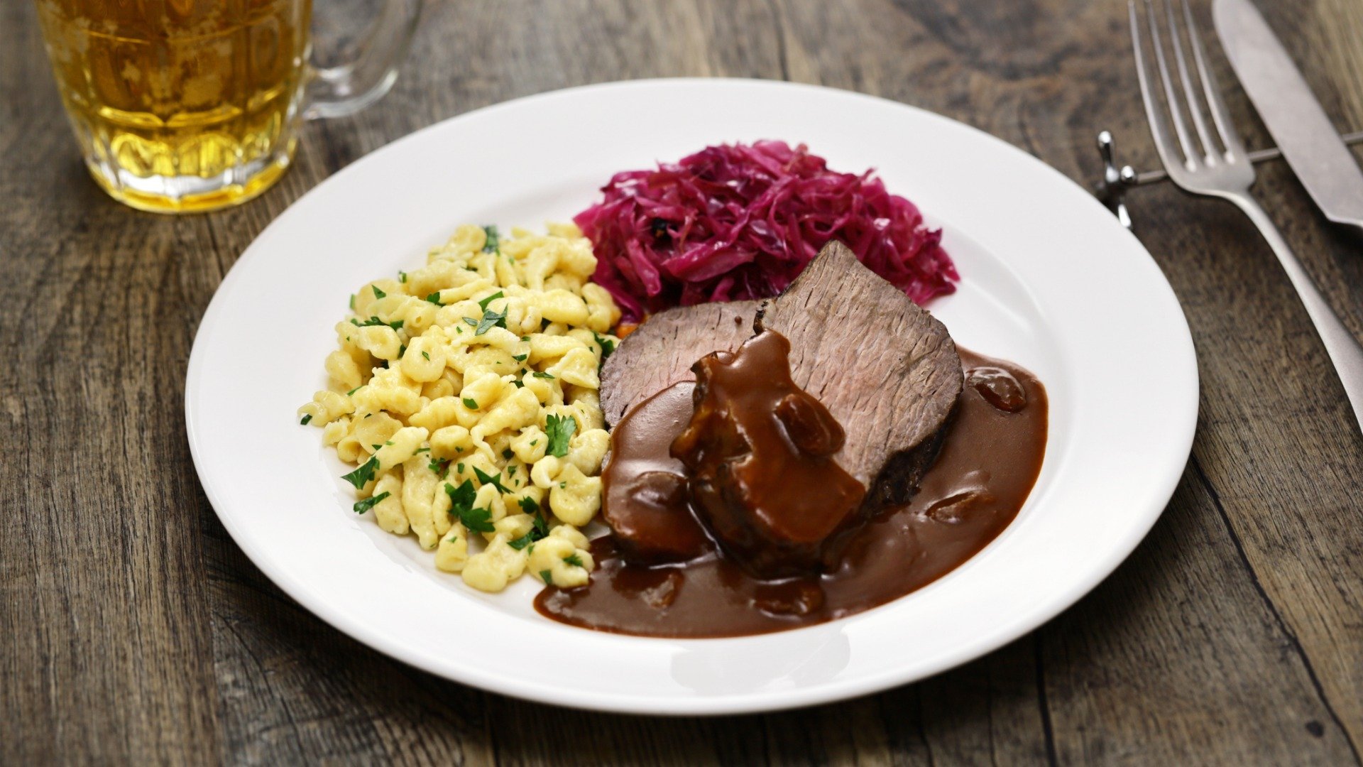 A white plate with slices of meat, red cabbage and Spatzle.